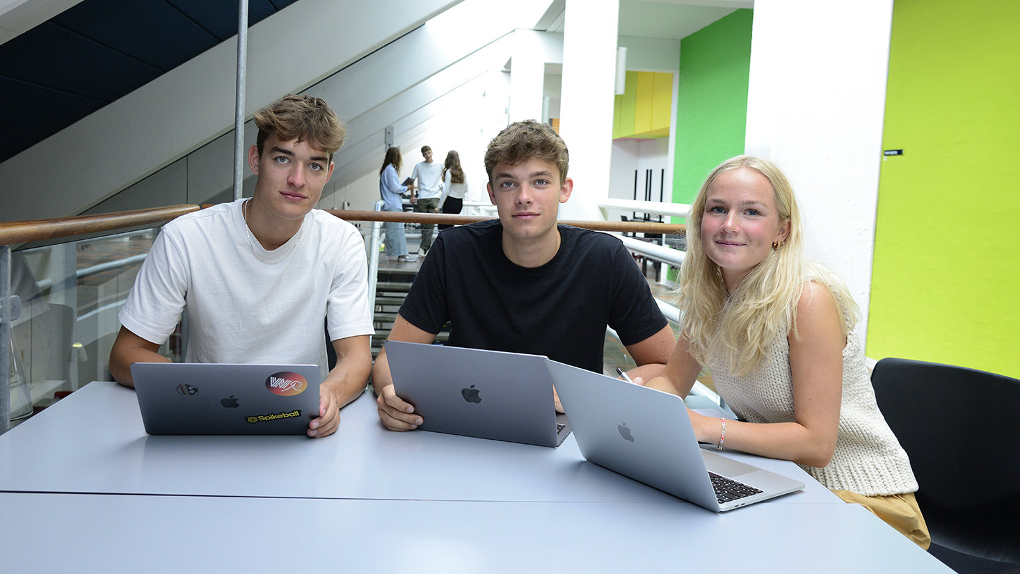 Tre unge studerende med bærbare computere.